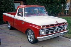 an old red and white pickup truck parked on the side of the road in front of a house