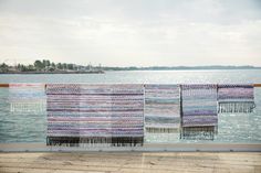 three colorful rugs hanging on the side of a wooden deck next to an ocean