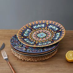 a stack of colorful plates sitting on top of a wooden table next to a knife and fork