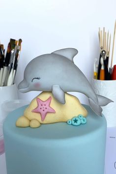 a blue cake with a dolphin and starfish on it's top, surrounded by paintbrushes