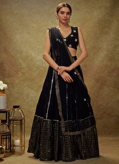 Embrace timeless elegance with the Black Mirror and Sequin Embroidered Lehenga set, a perfect blend of traditional allure and contemporary sophistication. Crafted from luxurious georgette, the flowing black lehenga is adorned with intricate gota and mirror work buttis, cascading gracefully into a striking sequin and zari embroidered border. Paired with a beautifully designed blouse, featuring mirror-embroidered buttis and accented with delicate pearl and mirror edges, this ensemble exudes opulence. The look is completed with a net dupatta, embellished with matching buttis and a coordinating border, adding an extra layer of grace. Designed for both style and convenience, this set includes a cancan for added volume and pockets for practicality, making it an ideal choice for Cocktail parties, Wedding Black Pre-draped Saree With Intricate Embroidery, Fitted Anarkali Set With Cutdana For Evening, Fitted Evening Anarkali Set With Cutdana, Fitted Cutdana Anarkali Set For Evening, Designer Black Anarkali Set With Cutdana, Black Anarkali Set With Cutdana For Designer Wear, Elegant Evening Anarkali Set With Cutdana, Black Dress With Pallu For Evening, Black Sharara For Reception During Navratri