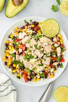 a white bowl filled with chicken salad next to sliced avocado and limes