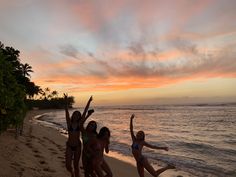 three girls are jumping on the beach at sunset with their arms up in the air