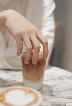 a person reaching for something in a cup on a table with a coffee cappuccino