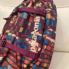 a colorful backpack sitting on top of a white couch in front of a pillow with the word'shopboom'written on it