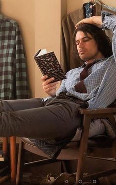 a man sitting in a chair holding a book while wearing a tie and dress shirt