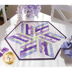 a quilted table runner with purple and green strips on it, next to a potted plant