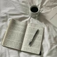 a cup of coffee and an open book on top of a bed with writing in it