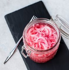 a jar filled with red onions sitting on top of a black place mat next to a fork