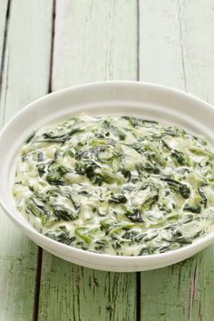 a white bowl filled with spinach and cheese on top of a green tablecloth