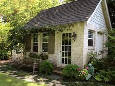 a small white brick house with green shutters and flowers on the front porch area