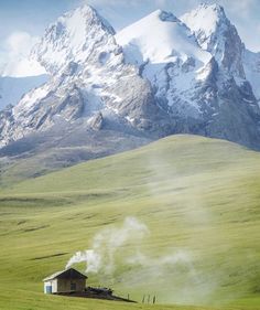 an old farm house in the middle of a green field with mountains in the background