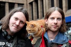 two men standing next to each other with a cat on their shoulders