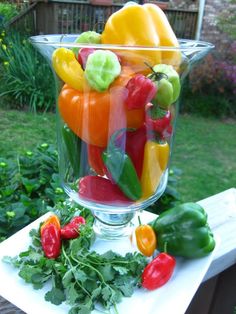 a glass vase filled with lots of different types of fruits and vegetables sitting on top of a wooden table