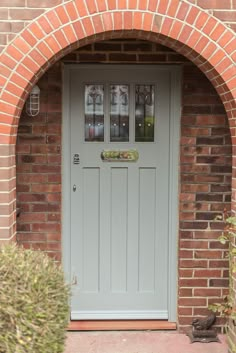 a grey front door with glass panes on the side and brick arch above it