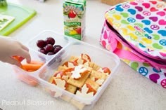 a lunch box with crackers, fruit and yogurt on the table next to it