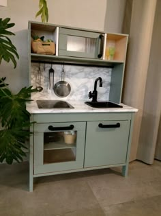 a small green kitchen with a sink and cupboards on the wall next to a potted plant