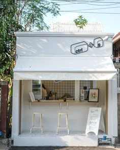 a small white building with two stools in front of it and a sign on the outside