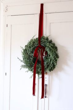 a wreath hanging on the front door with a red ribbon tied around it and a pair of scissors next to it