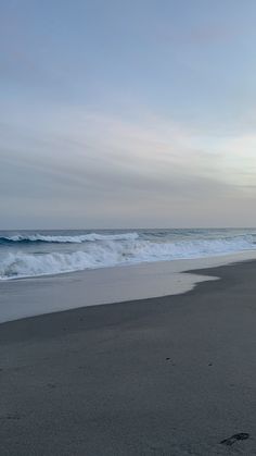 an empty beach with waves coming in from the ocean