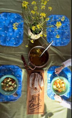 three people are eating food at a table with blue placemats and yellow flowers