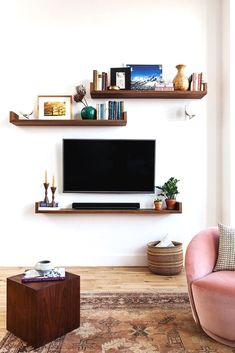 a living room with a tv and some shelves on the wall above it is a pink chair