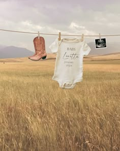 two baby onesuits hanging on a clothes line in a field