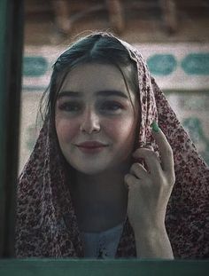 a woman with a scarf around her head talking on a cell phone in front of a mirror