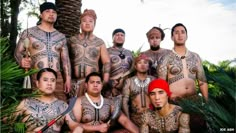 a group of men with tattoos on their bodies posing for a photo in front of some palm trees