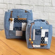 two denim bags sitting on top of a wooden table next to each other, one is blue and the other has white patchwork