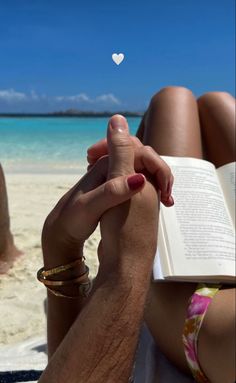 a person sitting on the beach reading a book with a white heart floating above them