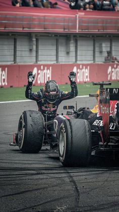 a red and black race car driving down a track with its arms in the air