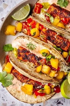 three fish tacos with mango salsa and lime wedges on a white platter