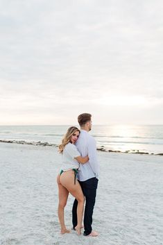 a man and woman are standing on the beach with their backs to each other as they hug