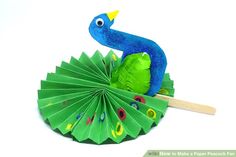 a paper peacock sitting on top of a green leaf