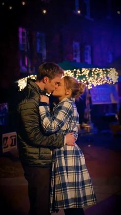 a man and woman kissing in front of christmas lights