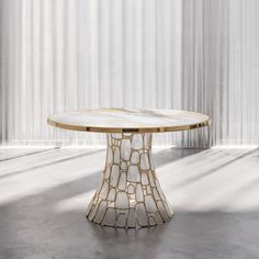 a round table with white marble top and gold trimmings on the base, in front of a curtained wall