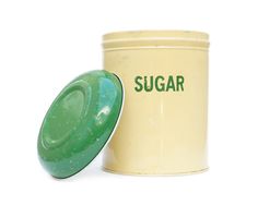 a green sugar container next to a white canister on a white background with the word sugar written below it