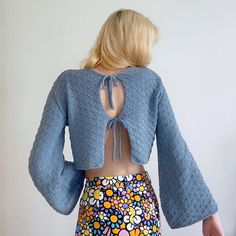 the back of a woman's crop top with flowers on it and an open knitted jacket over her shoulders