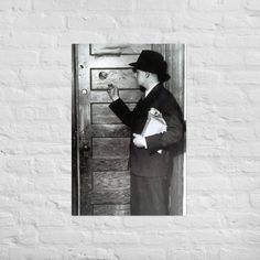 a black and white photo of a man wearing a hat holding a bag in front of a door