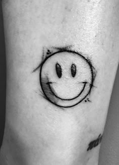 a black and white photo of a smiley face tattoo on the ankle with an arrow