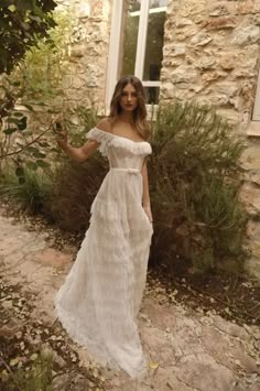 a woman standing in front of a stone building wearing a white dress and posing for the camera