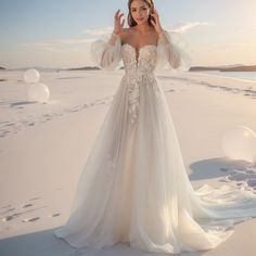 a woman standing on top of a sandy beach wearing a wedding dress with long sleeves