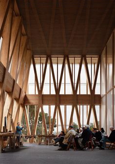 many people are sitting in chairs and tables inside the building with wooden beams on the ceiling