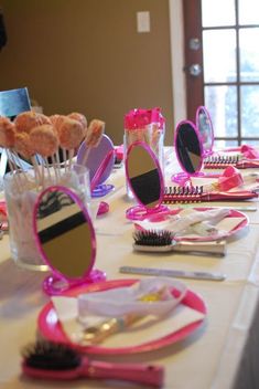 a table topped with lots of pink and white plates covered in makeup brushes next to a vase filled with donuts