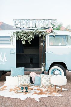 an old blue van is parked in front of a flower covered area with pillows and rugs