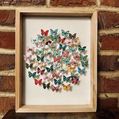 a wooden frame filled with colorful butterflies on top of a brick wall next to a brown brick wall