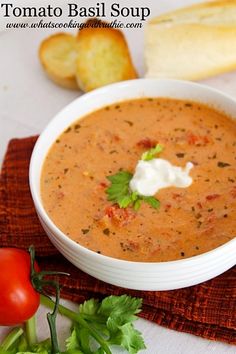 a white bowl filled with soup next to bread and tomatoes on a red place mat