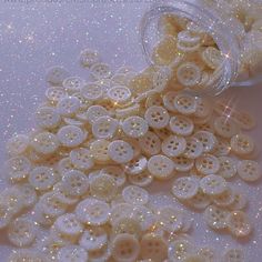 a jar filled with lots of white buttons sitting on top of a table covered in glitter