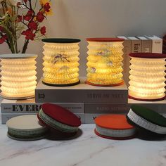 three lamps sitting on top of a table next to books and vases with flowers in them